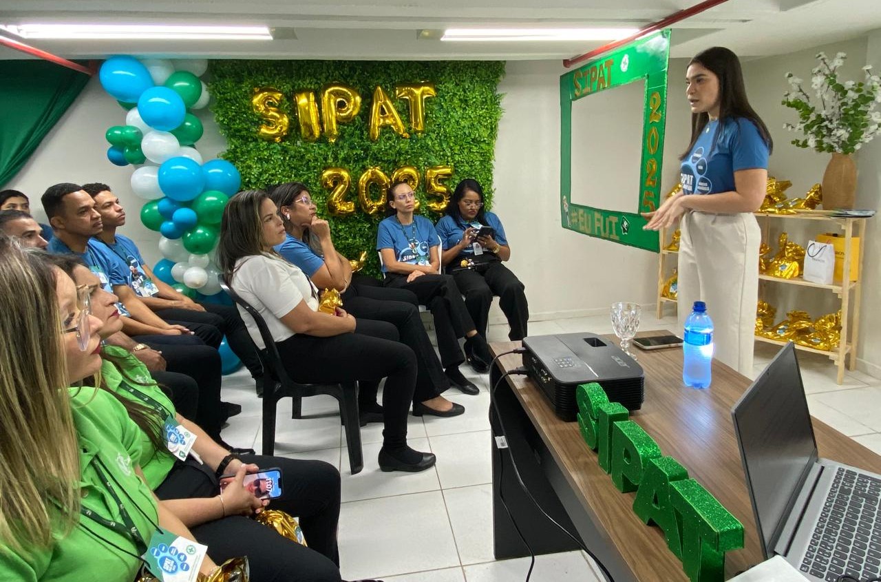 Fotografia tirada durante uma palestra ministrada por um advogada, existe um texto no fundo da imagem onde é possível ler em balões com forma de letras as palavras: "SIPAT 2025".