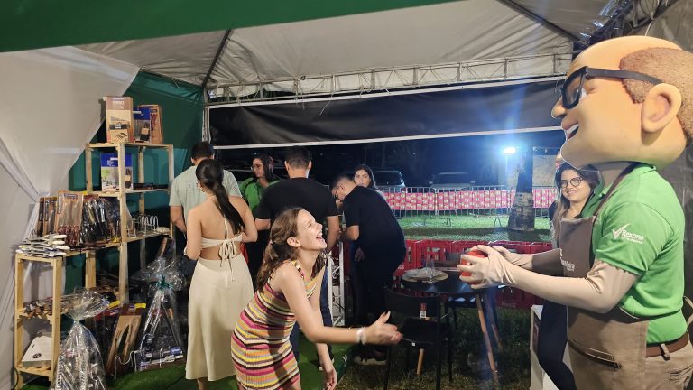 Foto do Vieião interagindo com uma criança que está rindo com a mão estandida como se estivesse cumprimentando Vieirão dentro do stand da Casa Vieira e Tramontina