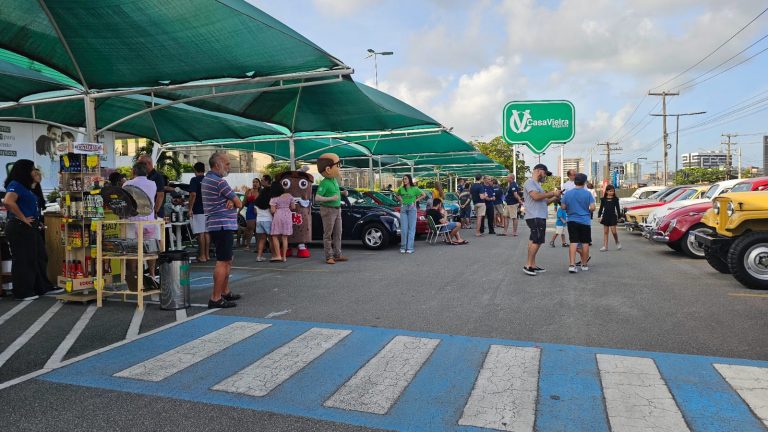 Foto paisagem do estacionamento da Casa Vieira - Praia onde há carros antigos estacionados com várias pessoas andando e observando.